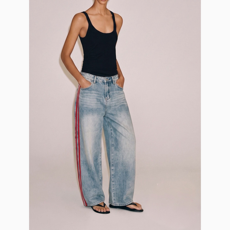 Modelo veste calças de ganga GRINE wide leg azul-claro com riscas laterais vermelhas e cintura subida.