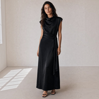 Modelo veste vestido longo acetinado preto GRINE com gola alta drapeada, sem mangas e faixa atada na cintura