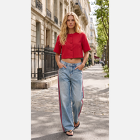 Modelo GRINE veste calças de ganga wide leg azul-clara com riscas laterais vermelhas em ambiente urbano.