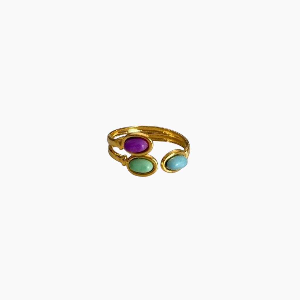 Anel GRINE ajustável em aço inoxidável dourado com três pedras ovais coloridas em tons de roxo, verde e azul.