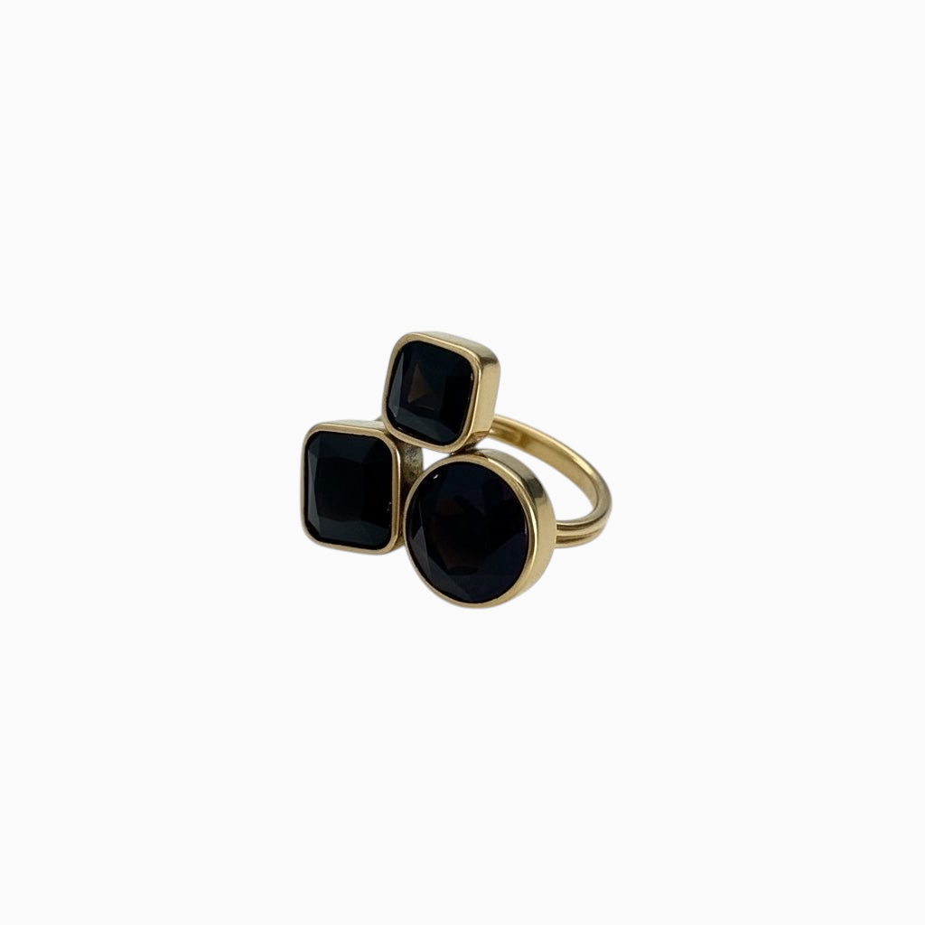 Anel GRINE em aço inoxidável dourado com três pedras pretas em formatos geométricos distintos