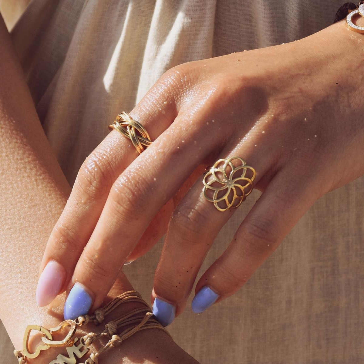 Anel GRINE com design de flor geométrica em acabamento dourado usado na mão de uma mulher com unhas coloridas.