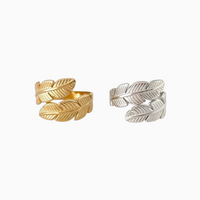 Anéis GRINE com design de folhas entrelaçadas em aço inoxidável, disponíveis em acabamento dourado e prateado.