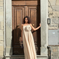 GRINE Mary beige cotton maxi dress with spaghetti straps and removable floral detail on bust. Model stands in front of a wooden door.