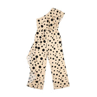 GRINE beige one-shoulder jumpsuit with black polka dots and elastic waist. Model holds a patterned clutch.