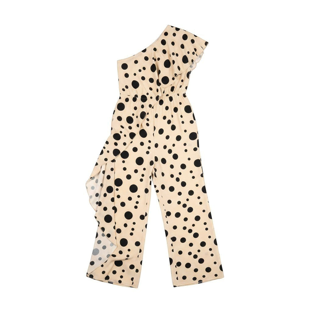 GRINE beige one-shoulder jumpsuit with black polka dots and elastic waist. Model holds a patterned clutch.