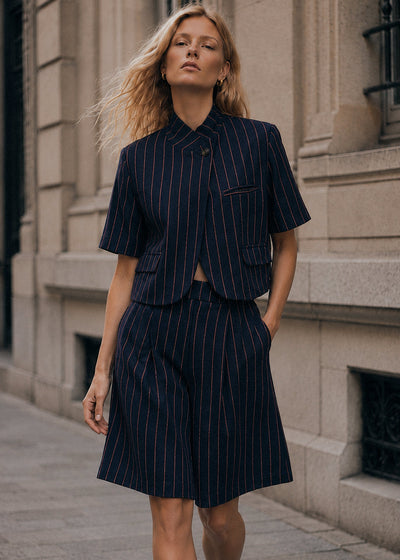 Modelo veste bermudas de alfaiataria GRINE azul-marinho com risca de giz, cintura subida e pregas, estilo urbano.
