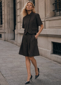 Modelo veste bermudas de alfaiataria GRINE risca de giz com pregas, cintura subida e corte largo em ambiente urbano.