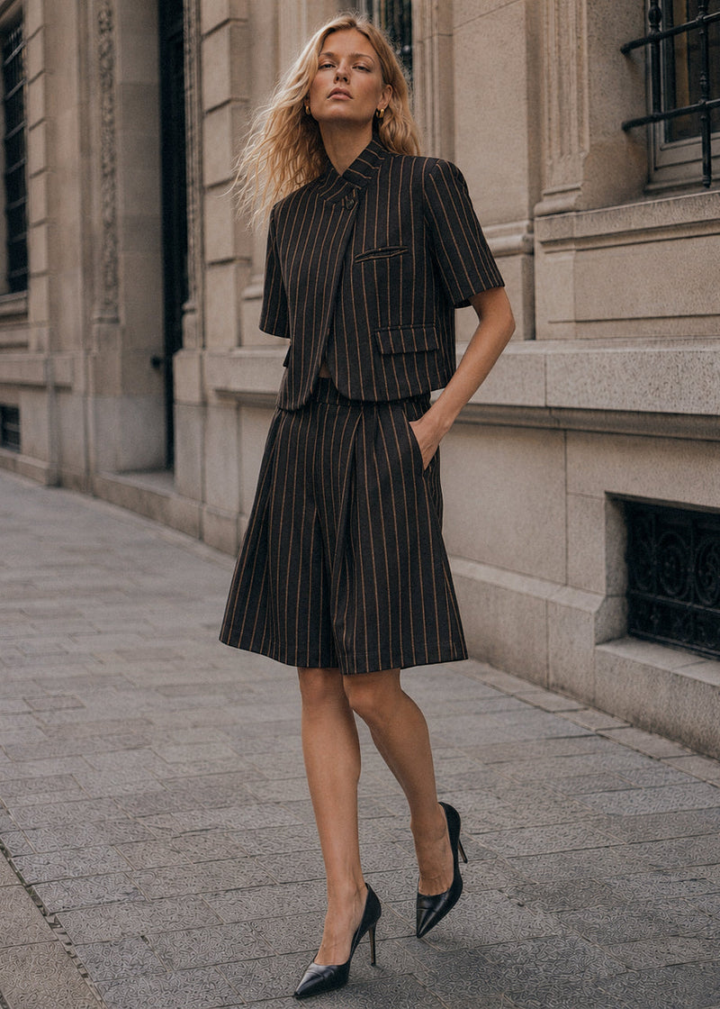 Modelo veste bermudas de alfaiataria GRINE com padrão risca de giz, cintura subida e corte largo em ambiente urbano.