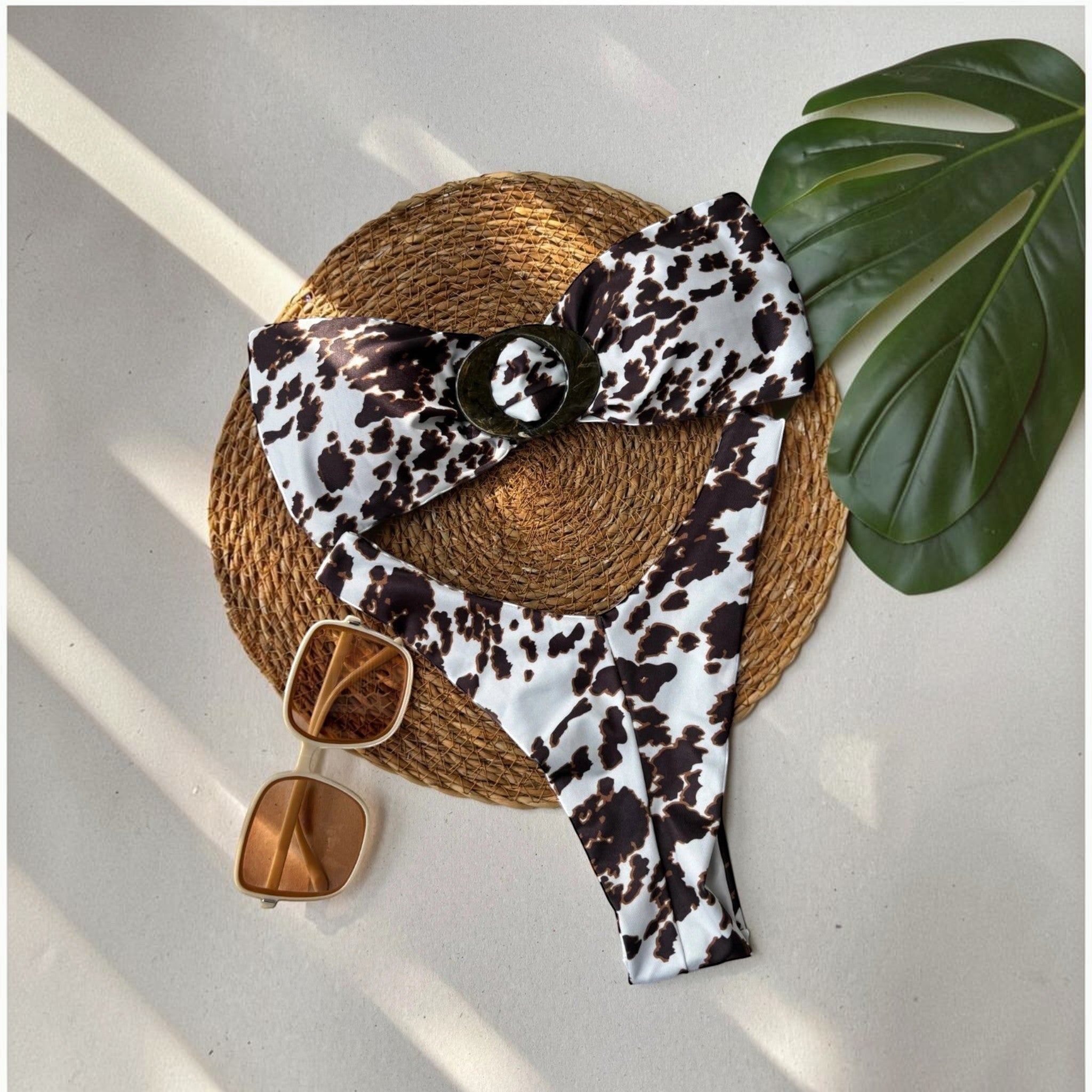 Biquíni GRINE com estampado cow print, modelo caicai e calcinha asa delta, sobre base de palha com óculos de sol.