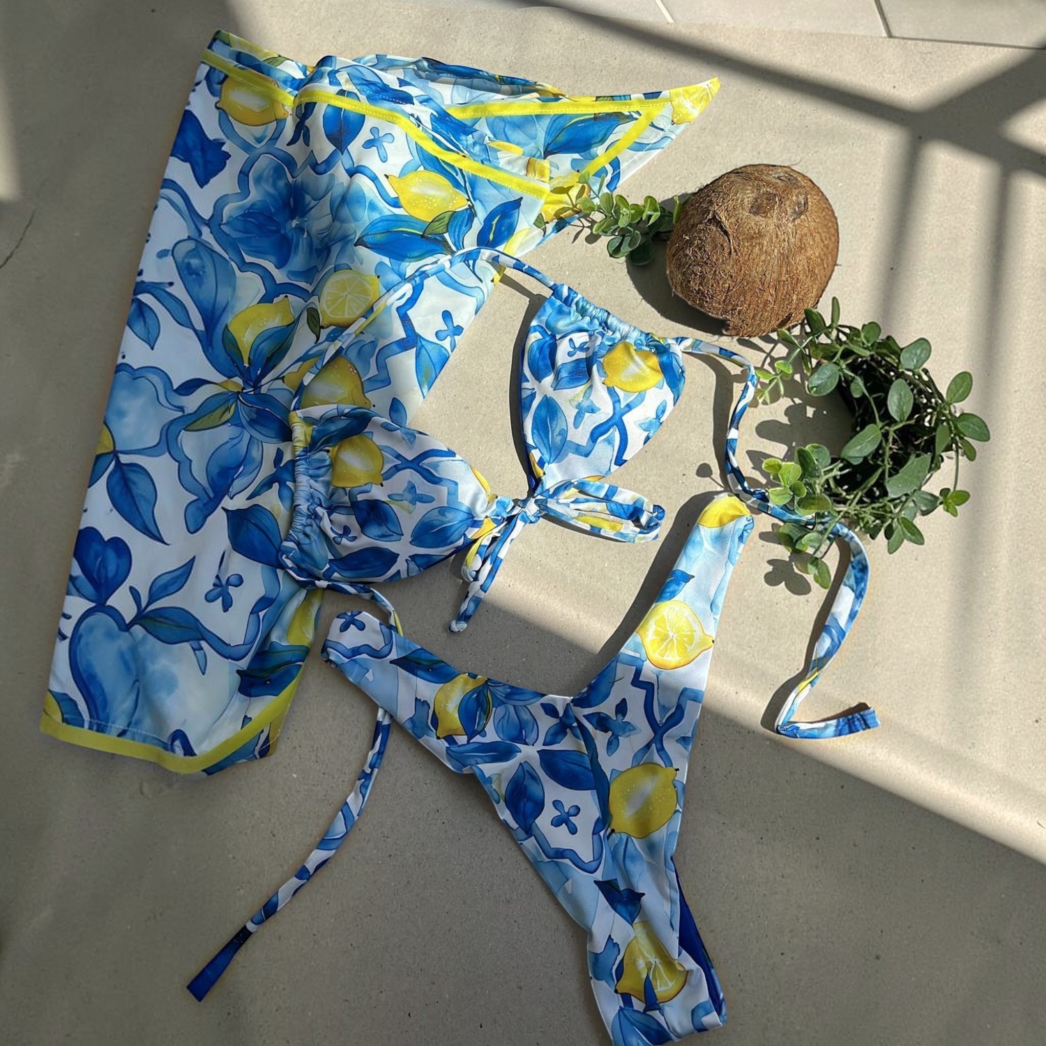 Biquíni GRINE Lemonade com estampa de limões amarelos e fundo azul, modelo cortininha e asa delta com canga a condizer.