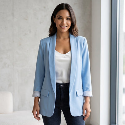 Mulher sorridente veste blazer aberto azul claro da GRINE com forro às riscas, sobre top branco e calças escuras.