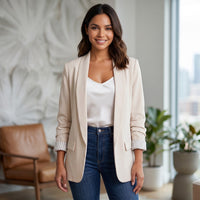 Mulher sorridente veste blazer aberto bege GRINE com forro de riscas, sobre top branco e calças de ganga.