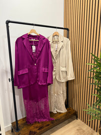 Blazer oversize acetinado GRINE em tons de roxo e bege, fluido com um botão e bolsos, exposto em cabides.
