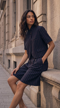 Modelo veste blazer cropped e bermudas de alfaiataria GRINE em azul-marinho com risca de giz num cenário urbano.