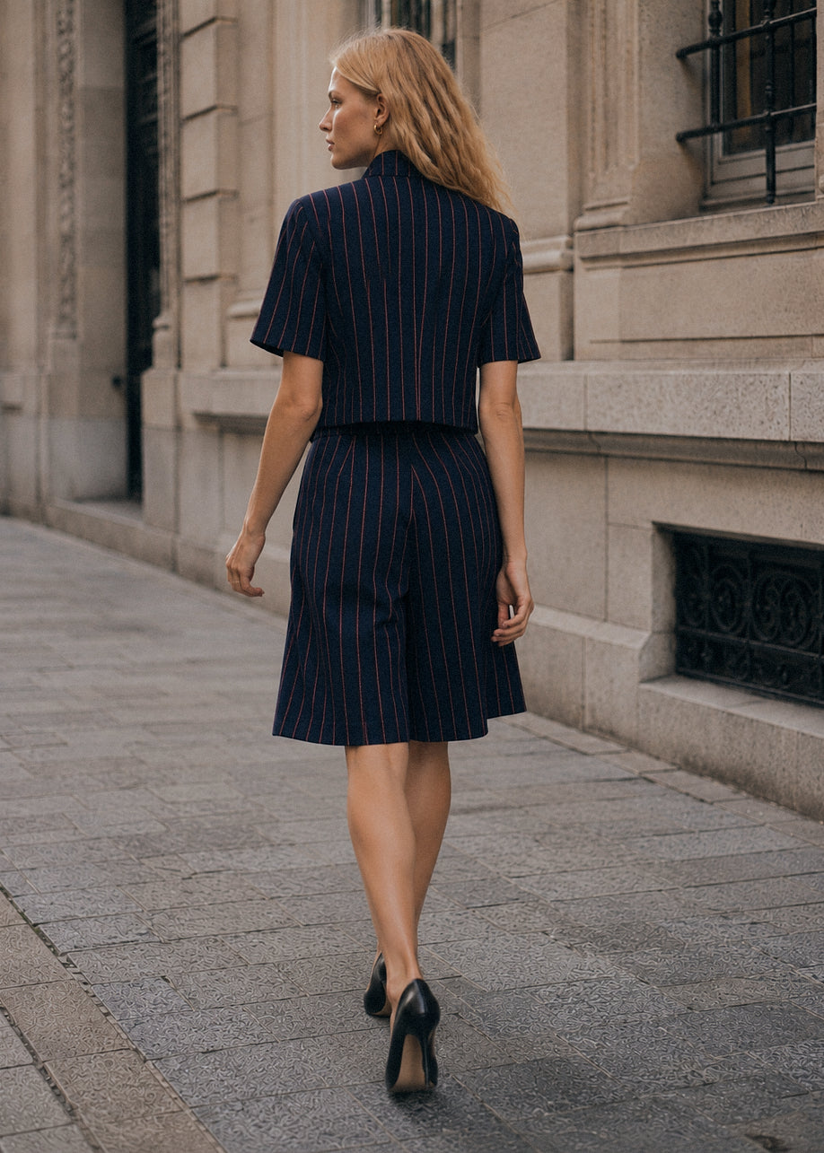 Modelo veste blazer cropped e bermudas GRINE em tecido azul marinho com risca de giz vermelha em ambiente urbano