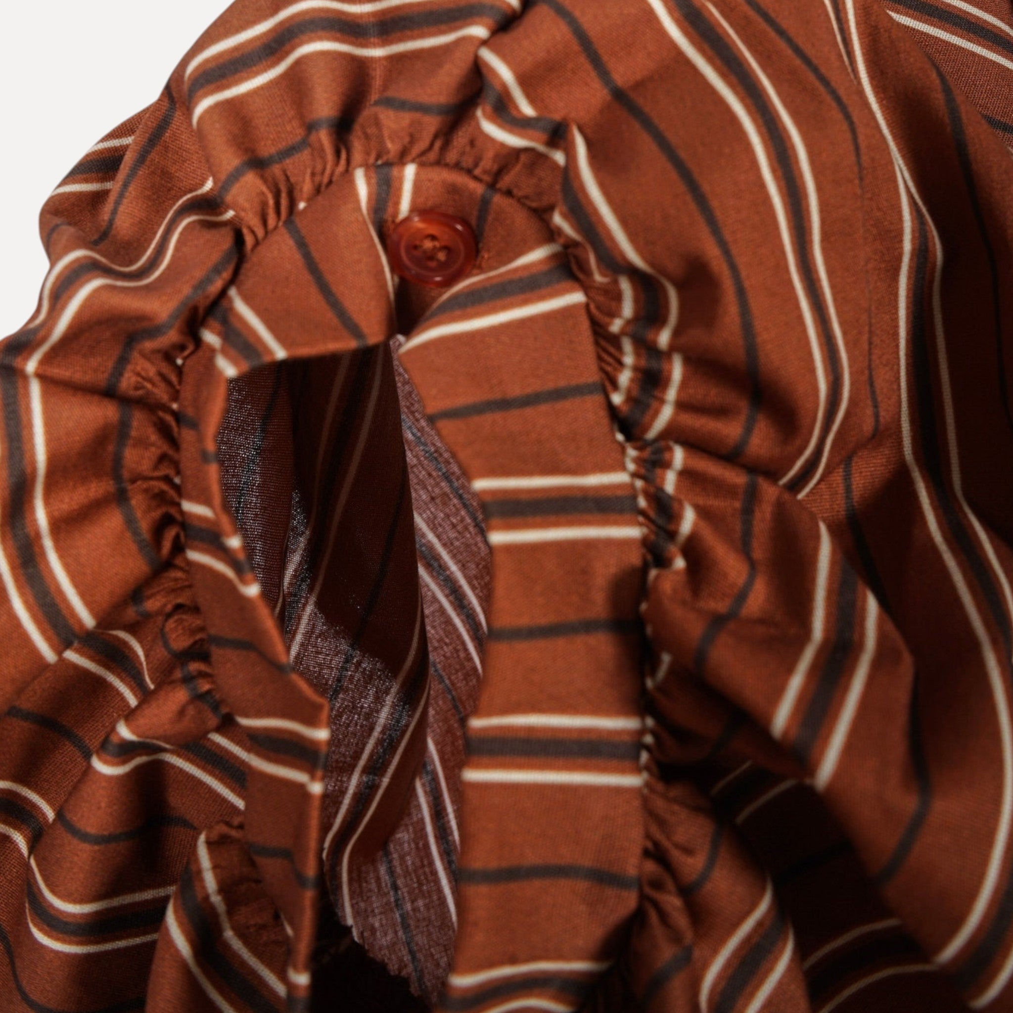 Detalhe do punho drapeado com botão da blusa listrada oversized GRINE em tom castanho e riscas brancas