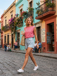 Modelo veste blusa GRINE às riscas cor-de-rosa com ombreiras e calções de ganga numa rua histórica e colorida.