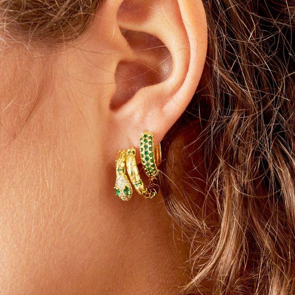 Brincos GRINE Desire em forma de argola com banho de ouro e zirconias verdes, usados na orelha de uma modelo.