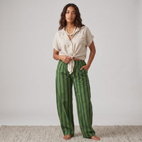 Modelo GRINE veste calças baggy de algodão com riscas verticais verdes e camisa bege de manga curta com nó frontal.