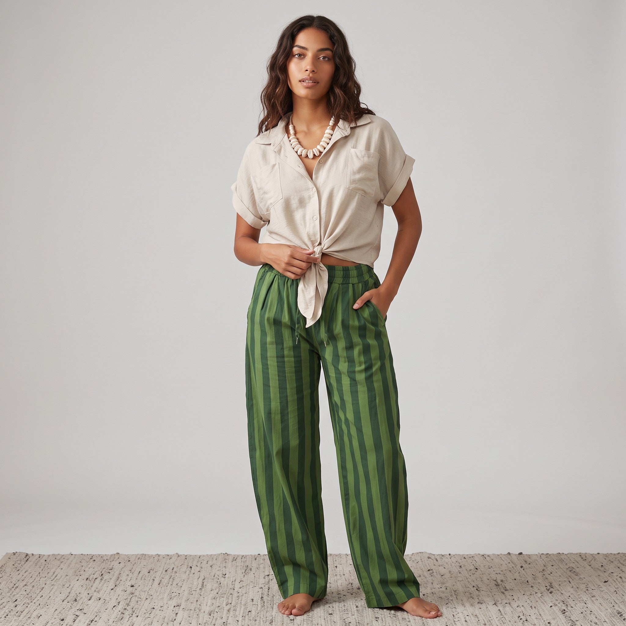 Modelo GRINE veste calças baggy de algodão com riscas verticais verdes e camisa bege de manga curta com nó frontal.