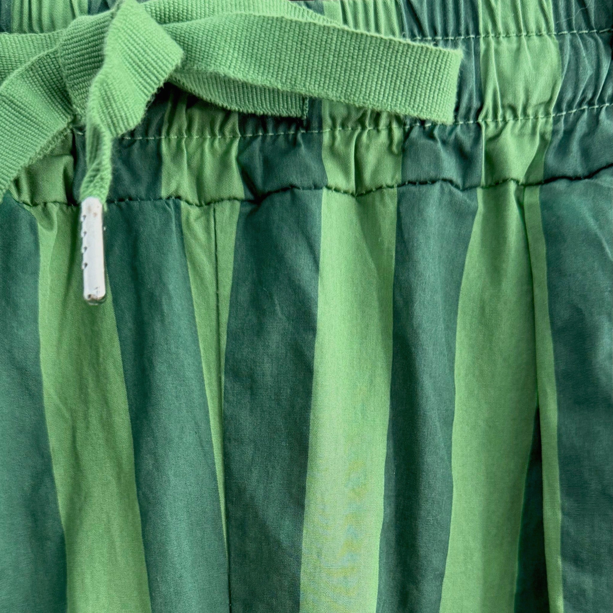 Detalhe da cintura de calças GRINE baggy em algodão com riscas verticais verdes e cordão de ajuste no mesmo tom.