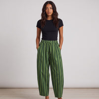 Modelo veste calças baggy GRINE às riscas verdes em algodão com cintura subida e pregas, estilo urbano e confortável.