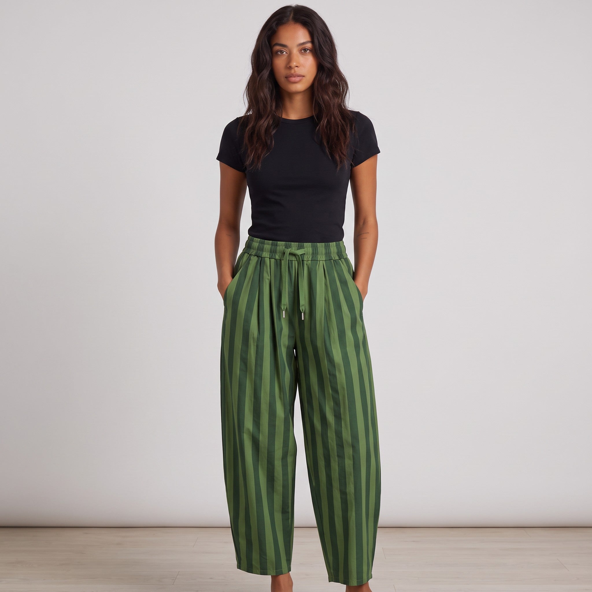 Modelo veste calças baggy GRINE às riscas verdes em algodão com cintura subida e pregas, estilo urbano e confortável.