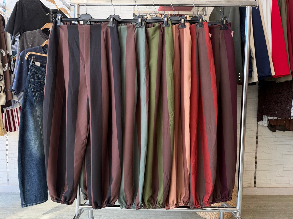 Calças balão GRINE com padrão às riscas em tons de verde militar, camel e tijolo, com cintura elástica e bolsos.