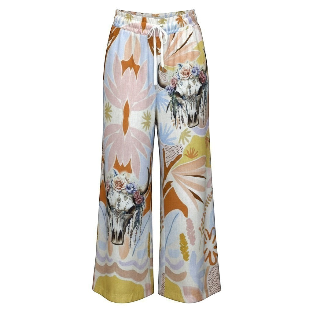 Calças Carmen GRINE de perna larga com estampado artístico tropical, caveiras florais e padrão abstrato em tons suaves. Cintura elástica com cordão.