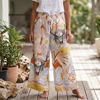 Calças Carmen GRINE de perna larga com estampado de caveira de touro e flores em tons pastel, cintura elástica com cordão. Look boho.