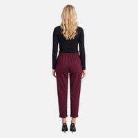 Vista traseira de modelo com calças chino GRINE bordeaux de corte fluido, cintura elástica e bainha dobrada.