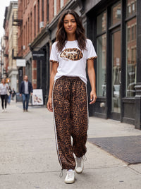 Modelo veste calças jogger GRINE oversized com padrão leopardo, riscas laterais brancas e bainhas ajustáveis na rua.