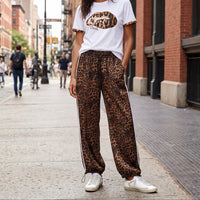 Modelo veste calças jogger GRINE oversized com padrão leopardo, riscas laterais brancas e bainhas ajustáveis na rua.