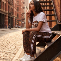 Modelo GRINE sentada em escadas de metal usando calças jogger oversized de viscose com padrão leopardo e riscas