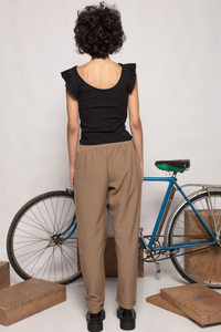 Modelo de costas vestindo calças jogger GRINE cor taupe com cintura elástica, combinadas com top preto e bicicleta.
