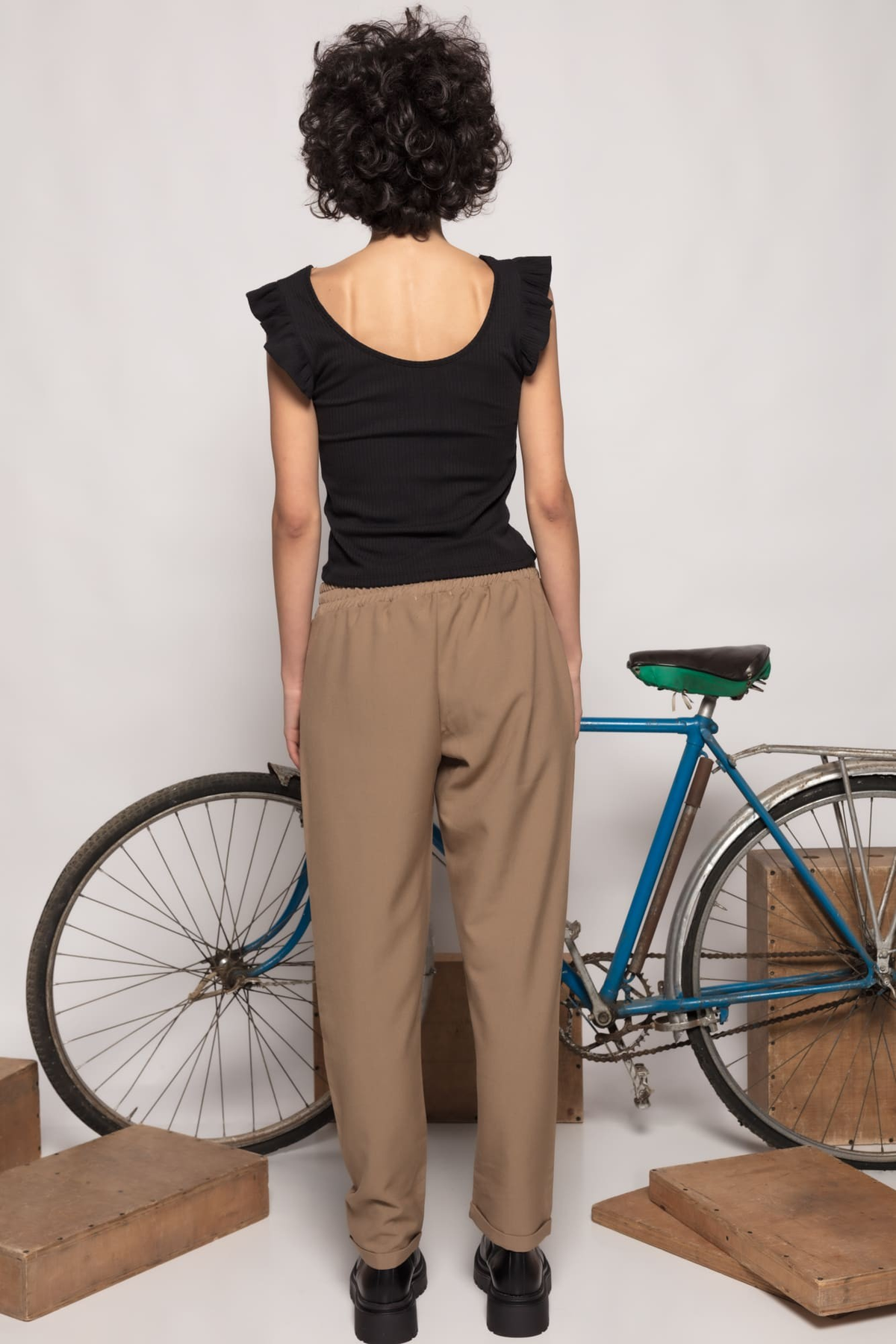 Modelo de costas vestindo calças jogger GRINE cor taupe com cintura elástica, combinadas com top preto e bicicleta.