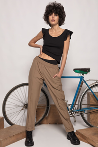 Modelo veste calças jogger GRINE cor taupe de cintura alta com elástico, combinadas com top preto e botas.