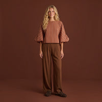 Modelo loira veste calças pantalona fluidas castanhas da GRINE com blusa às riscas e sapatos confortáveis.