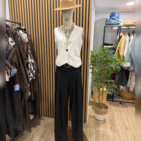Calças pantalonas pretas GRINE com perna larga e cintura elástica, exibidas em manequim com colete bege e chapéu.