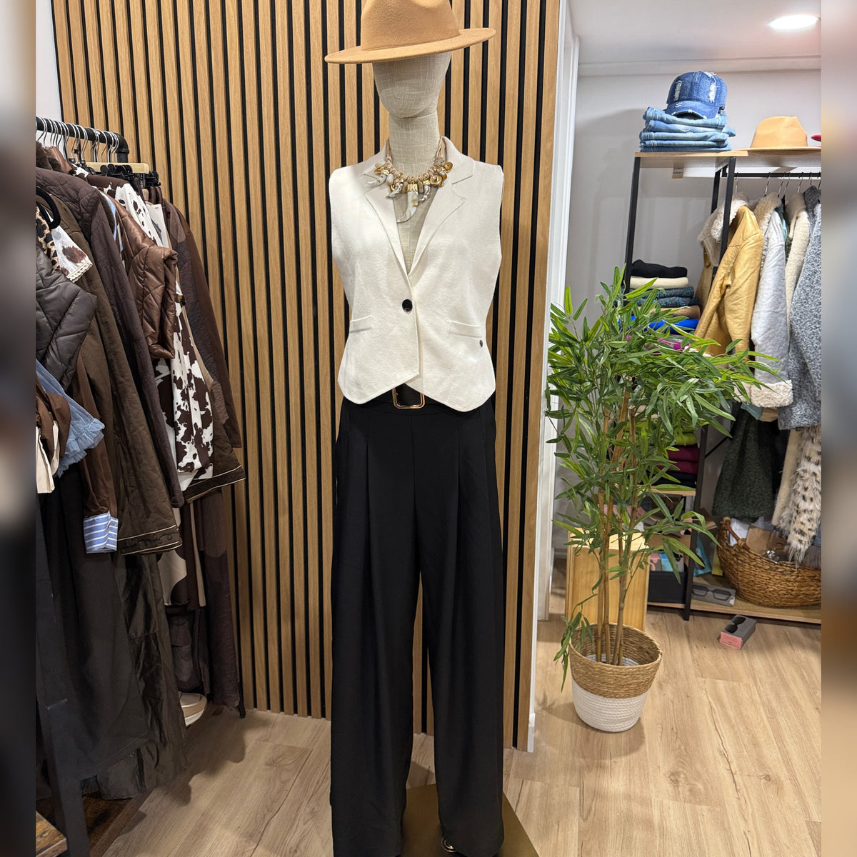 Calças pantalonas pretas GRINE com perna larga e cintura elástica, exibidas em manequim com colete bege e chapéu.