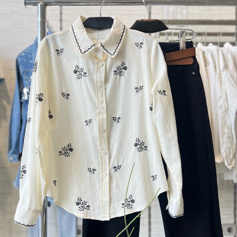 Camisa GRINE branca de algodão com bordados florais pretos e gola recortada, exibida num cabide.