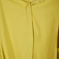 Detalhe da carcela oculta de camisa oversized GRINE em tecido fluido amarelo mostarda com acabamento minimalista