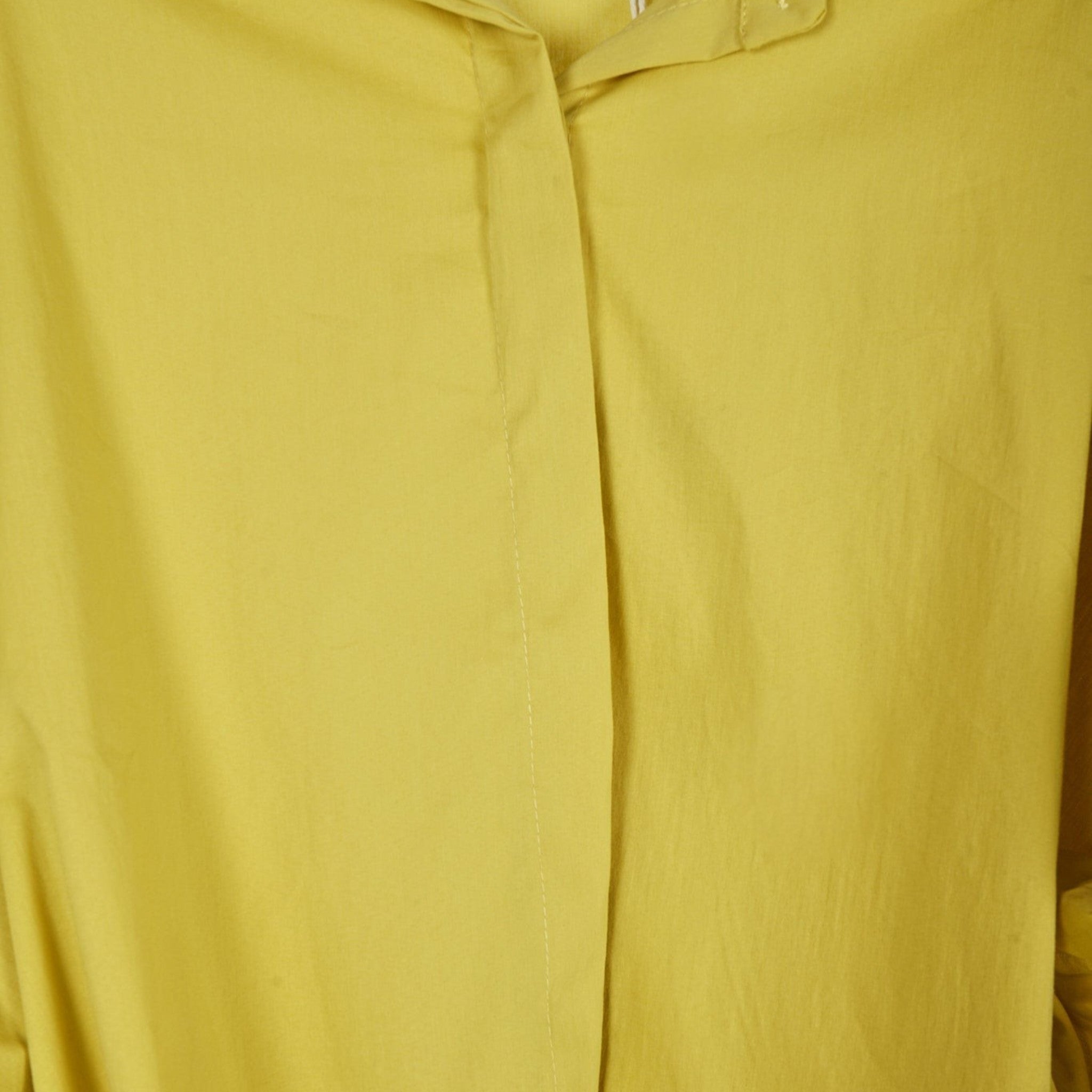 Detalhe da carcela oculta de camisa oversized GRINE em tecido fluido amarelo mostarda com acabamento minimalista