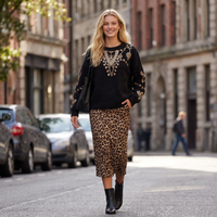 Modelo loira usa camisola de malha preta GRINE com lantejoulas e saia midi com padrão leopardo em rua urbana.