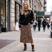 Modelo veste camisola de malha preta GRINE com lantejoulas, gola redonda e saia midi com padrão leopardo na rua.