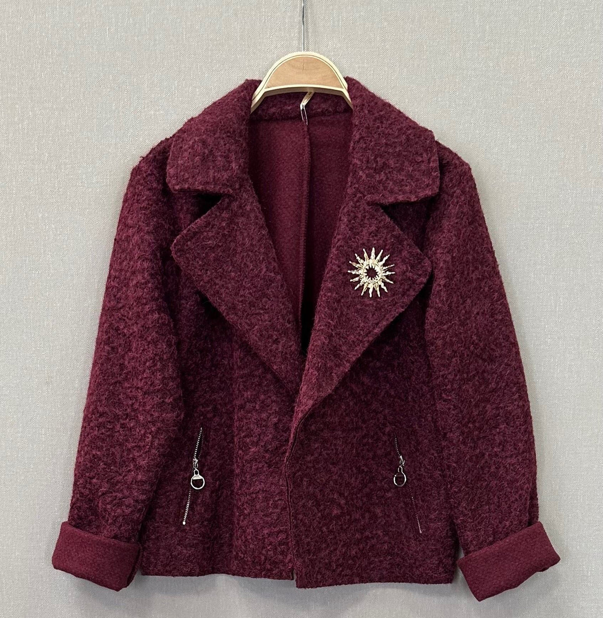 Casaco curto GRINE em tecido texturado bordeaux com gola de lapela, bolsos falsos e pregadeira decorativa dourada.