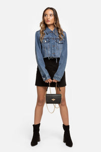 Modelo veste casaco de ganga curto azul da GRINE com gola, bolsos no peito e bainha desfiada, estilo casual.