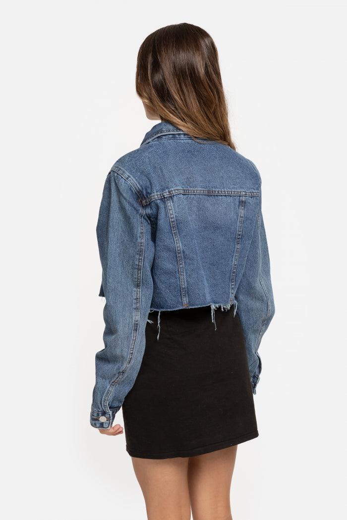 Casaco de ganga curto GRINE azul com corte reto, gola de camisa e bainha desfiada, visto de costas numa modelo.