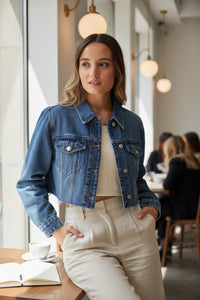 Modelo veste casaco de ganga curto azul da GRINE com gola de camisa e bolsos frontais em ambiente de café